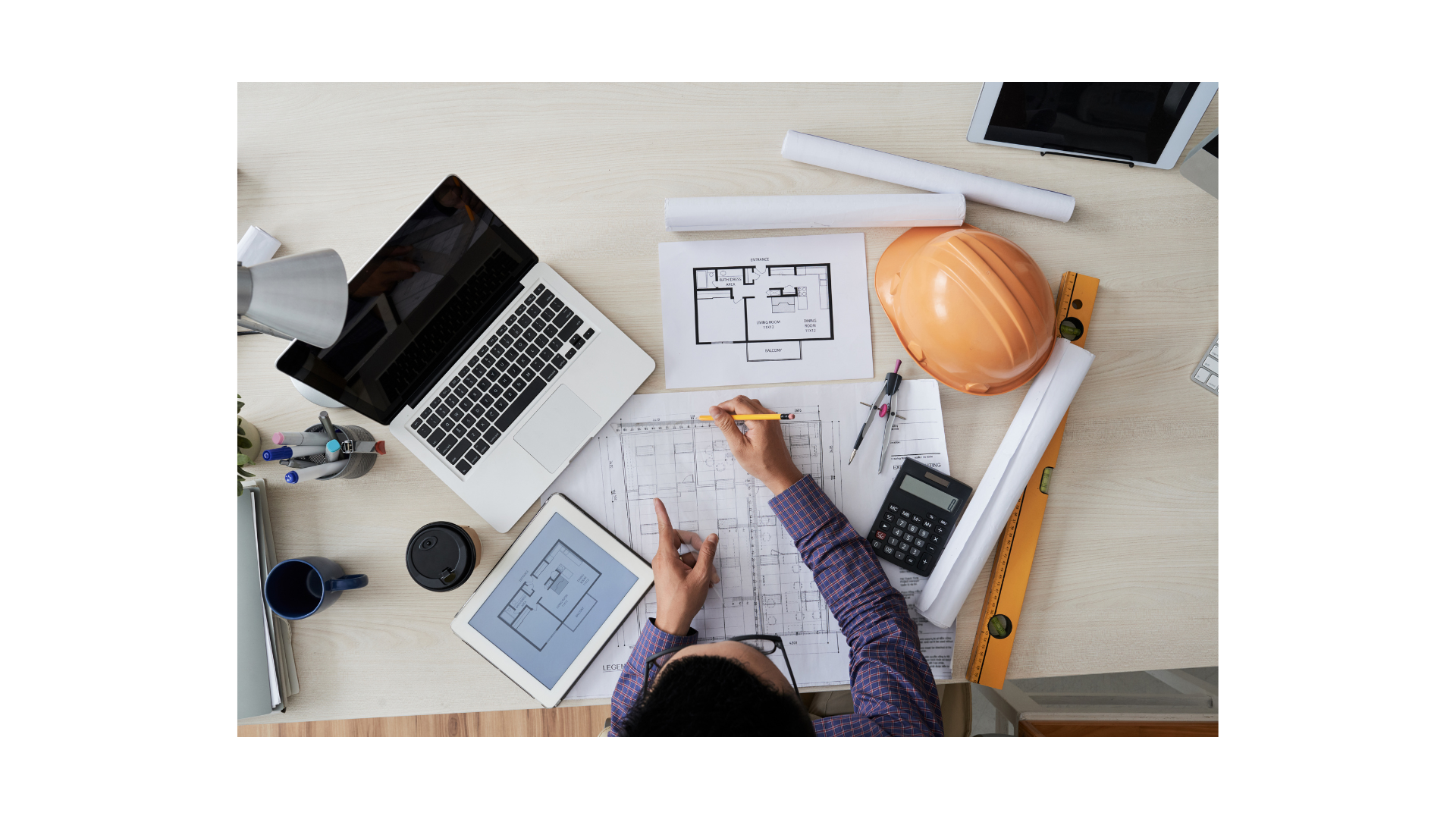 Mesa de trabalho com planta técnica, computador e capacete de engenharia